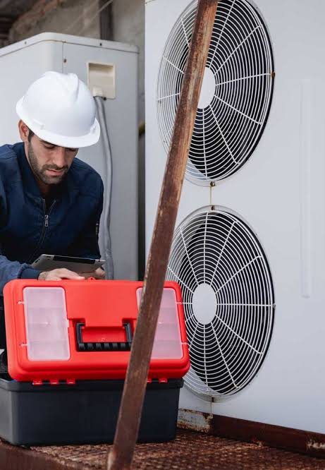 Technician using a tablet beside outdoor HVAC equipment and a toolbox